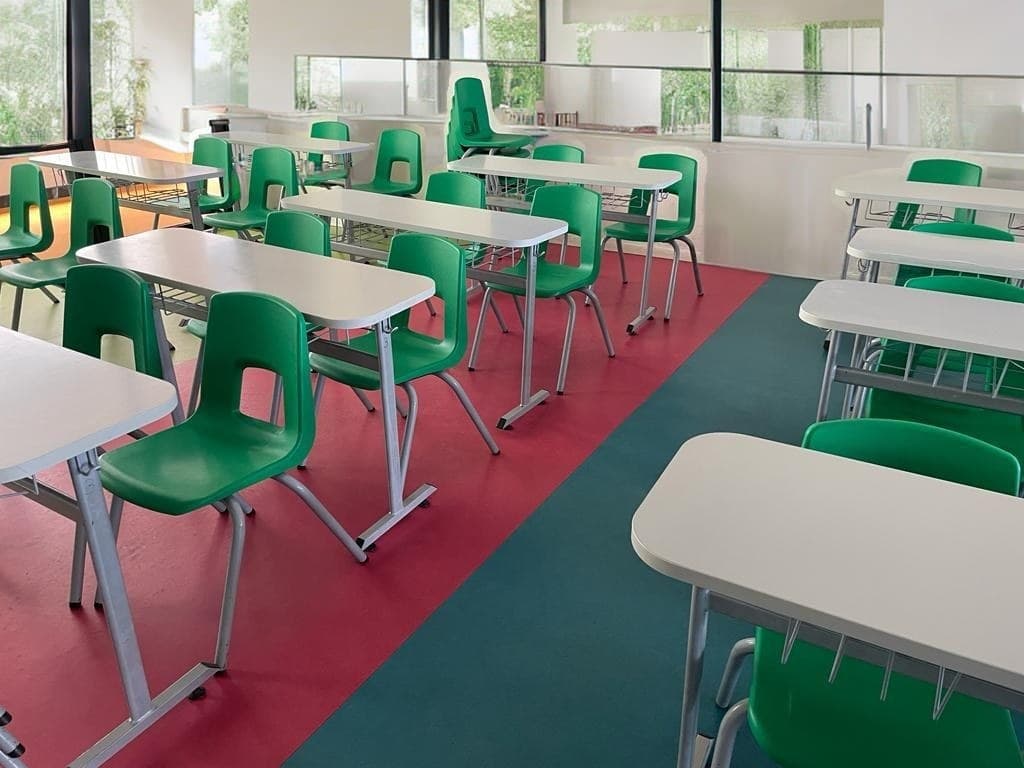 Two-seater classroom desks with green shell chairs in a daylit classroom — interior concept