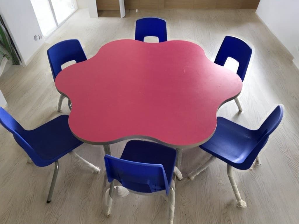 Pink petal-shaped table with six blue children’s chairs — interior concept